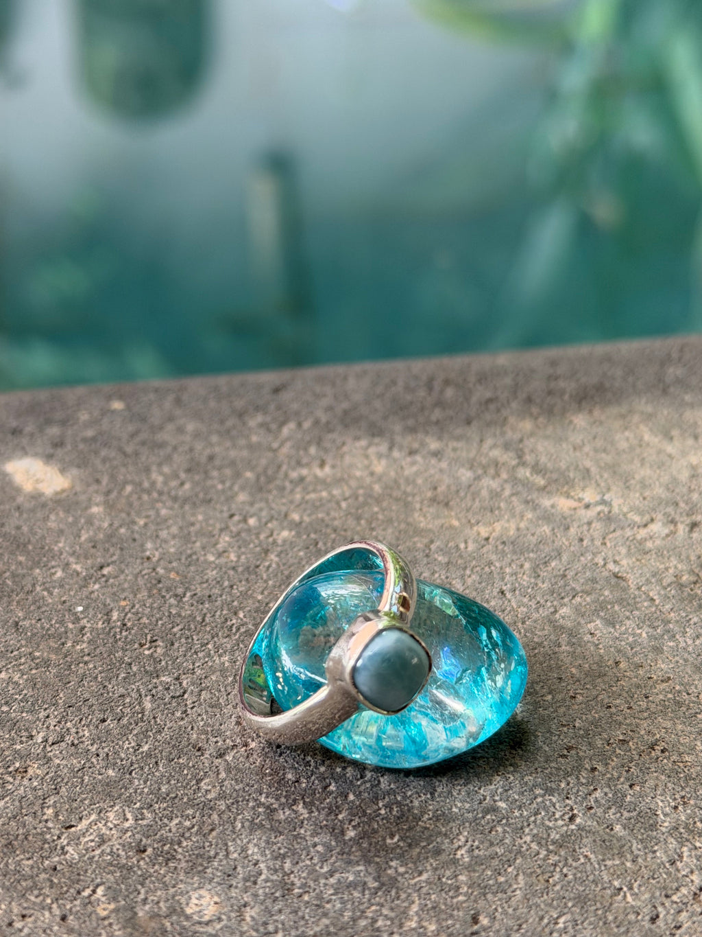 Blue glass ring with silver band on a concrete surface