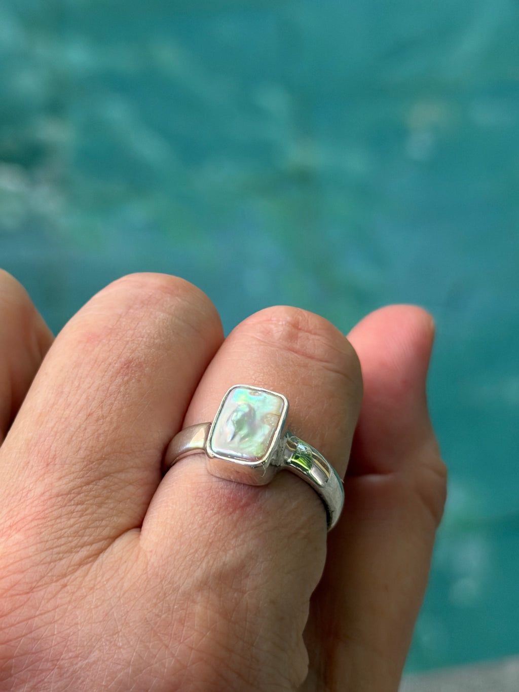 Hand wearing a silver ring with an pearl  against a blurred blue background