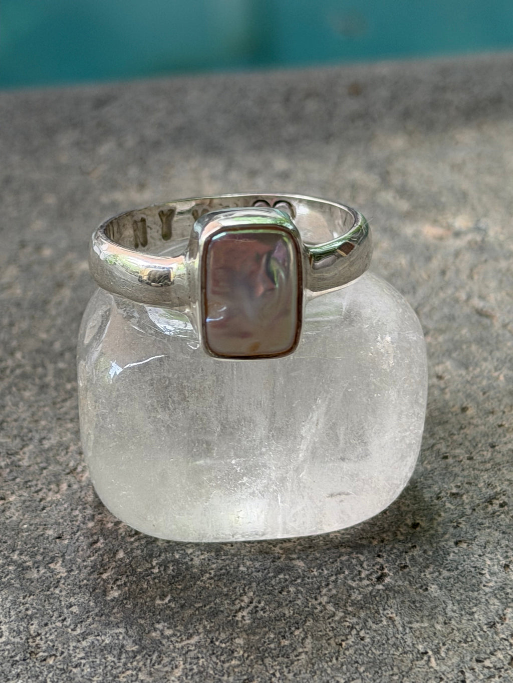 Silver ring with a square stone on a textured surface