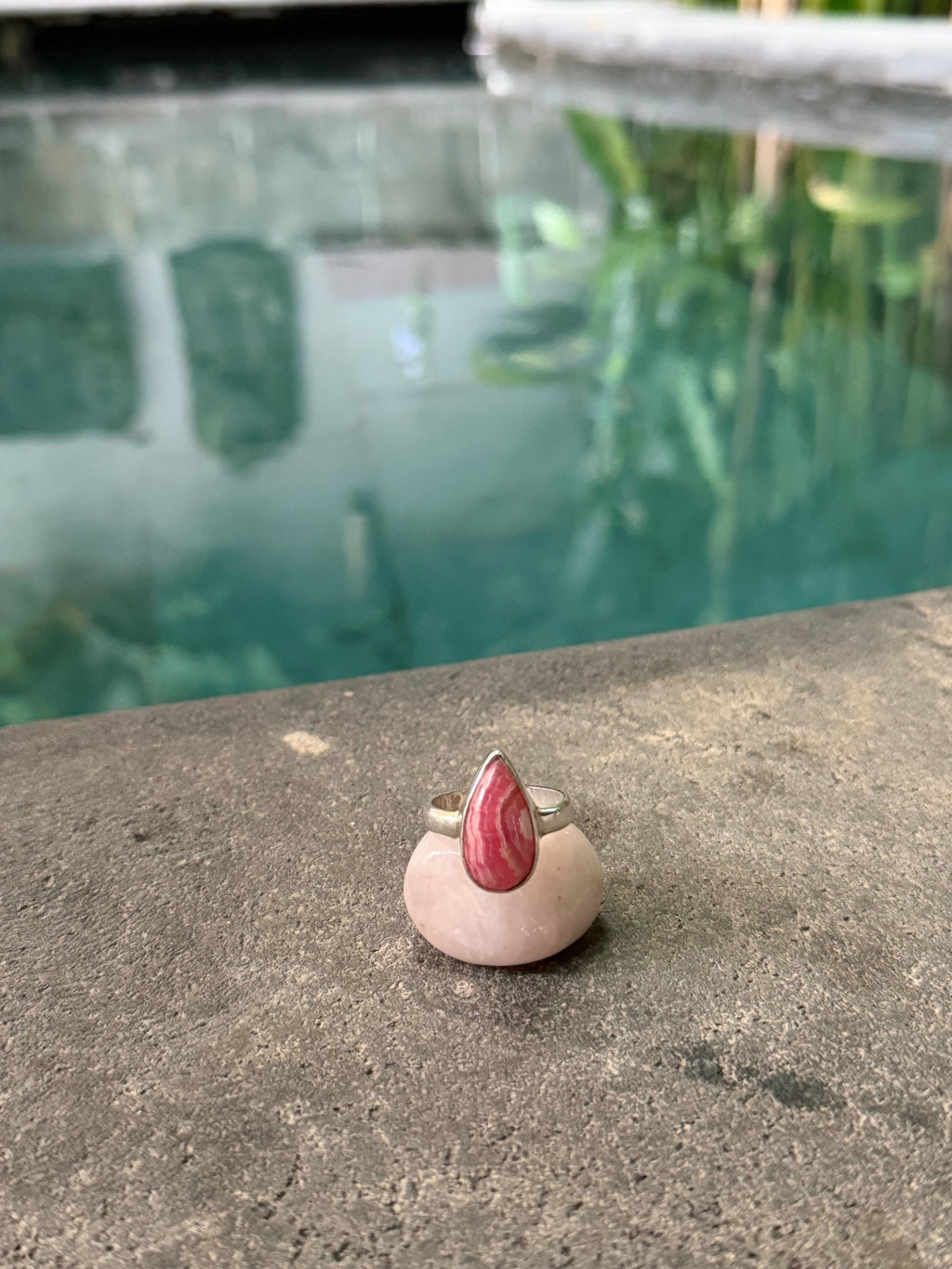 Small drop shaped ring with a Rhodochrosite stone on a concrete surface with a blurred background