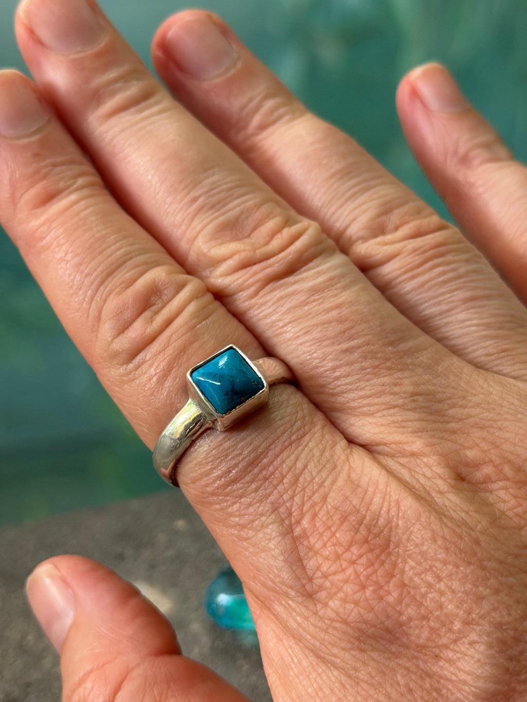 Hand wearing a ring with a blue stone against a blurred background